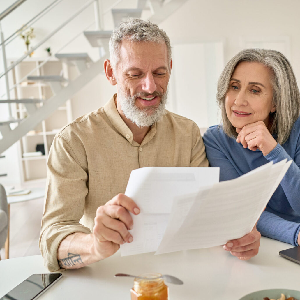 middle aged couple reading paper bills calculating pension using laptop at home.