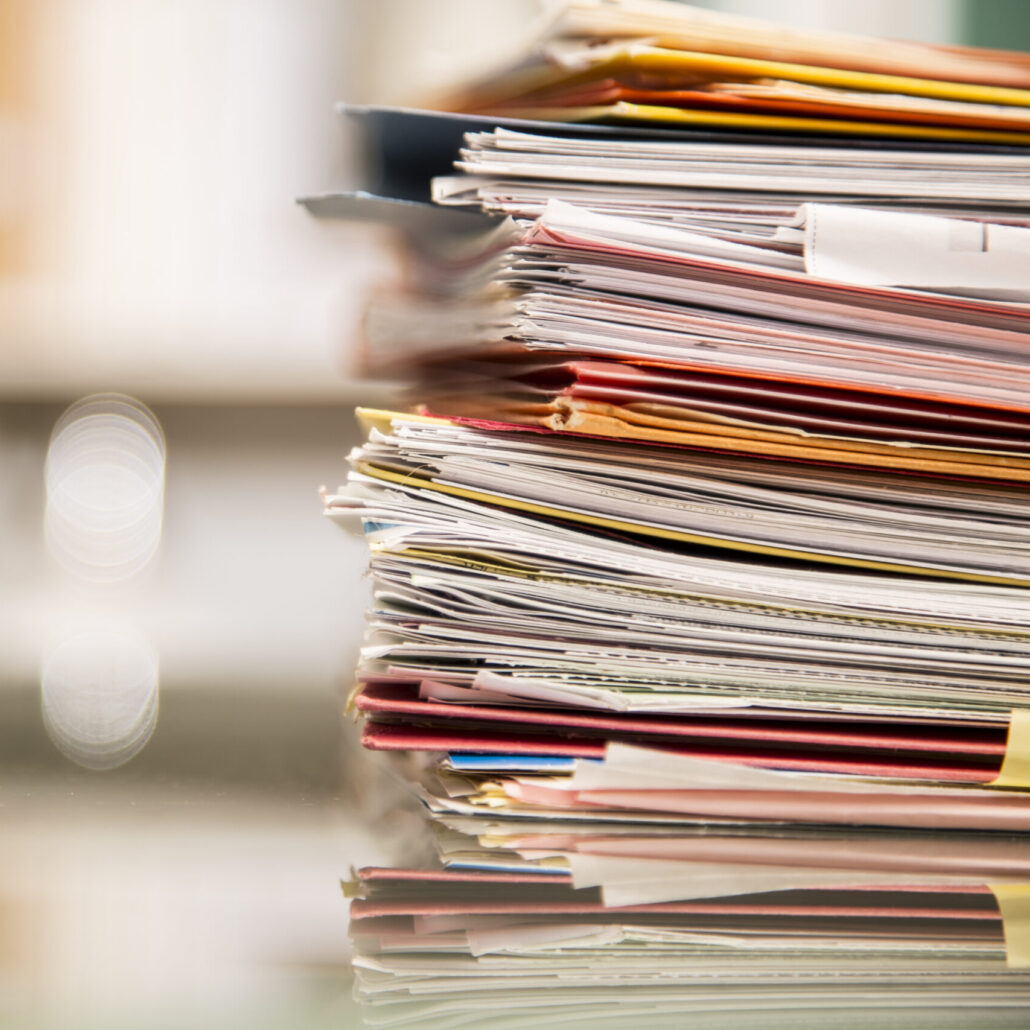 large stack of files, documents, paperwork on desk.
